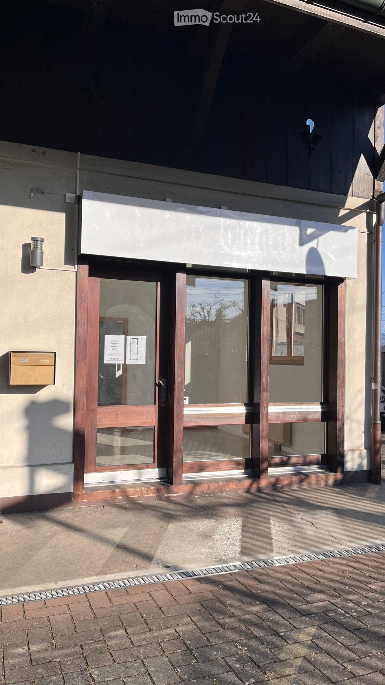 Storefront with glass doors and windows, wooden frame, beige wall, mounted light, mailbox