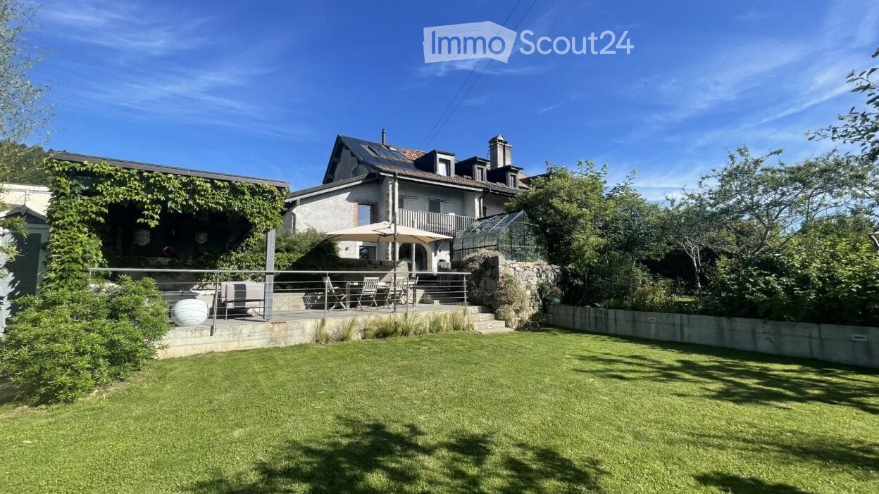 Well-maintained garden with a lawn, patio seating area, and a greenhouse attached to a house.