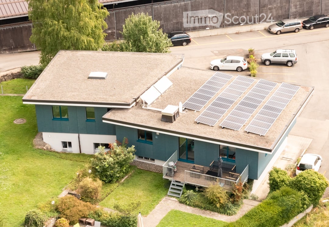 Blue house with solar panels on the roof, wooden deck with outdoor seating, multiple cars parked in the parking lot