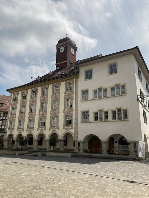Large building with many windows, clock tower, arched entrance, cobblestone courtyard