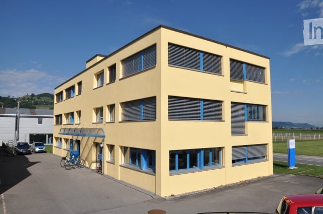 3 story building, yellow exterior, blue windows, parking lot, bicycles