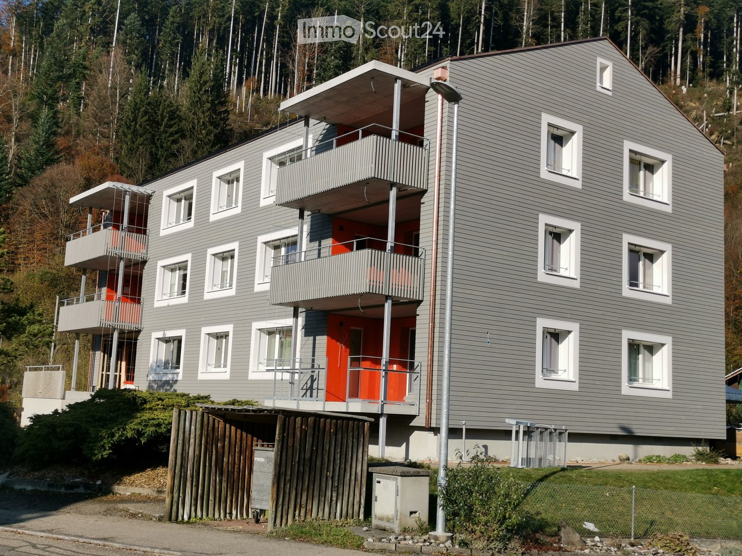 3 story apartment building, gray exterior, white windows, balconies, red doors, metal railings, street light