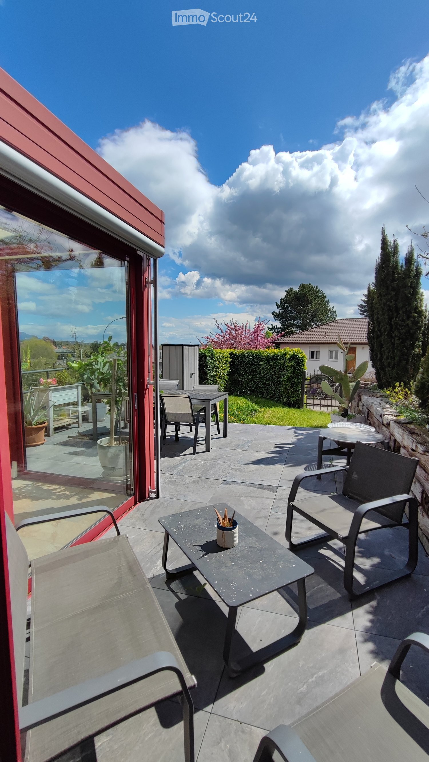 Outdoor patio with seating area, table, and potted plants, with a view of the surrounding landscape.
