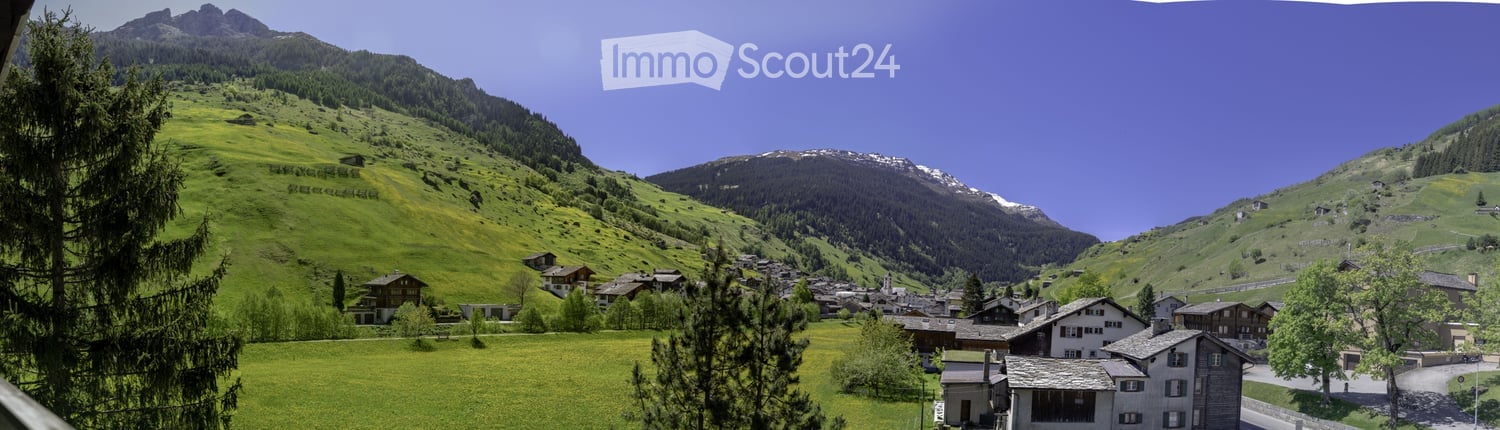 A picturesque alpine village with traditional houses nestled in a lush green valley surrounded by snow-capped mountains under a clear blue sky.