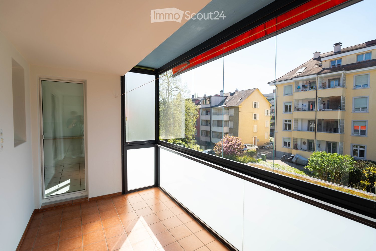 large glass windows, tiled floor, balcony, view of buildings and trees