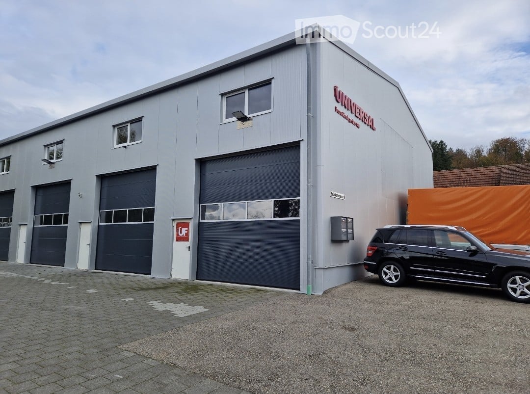 Industrial building with 4 garages, gray exterior, large windows, black SUV parked in front