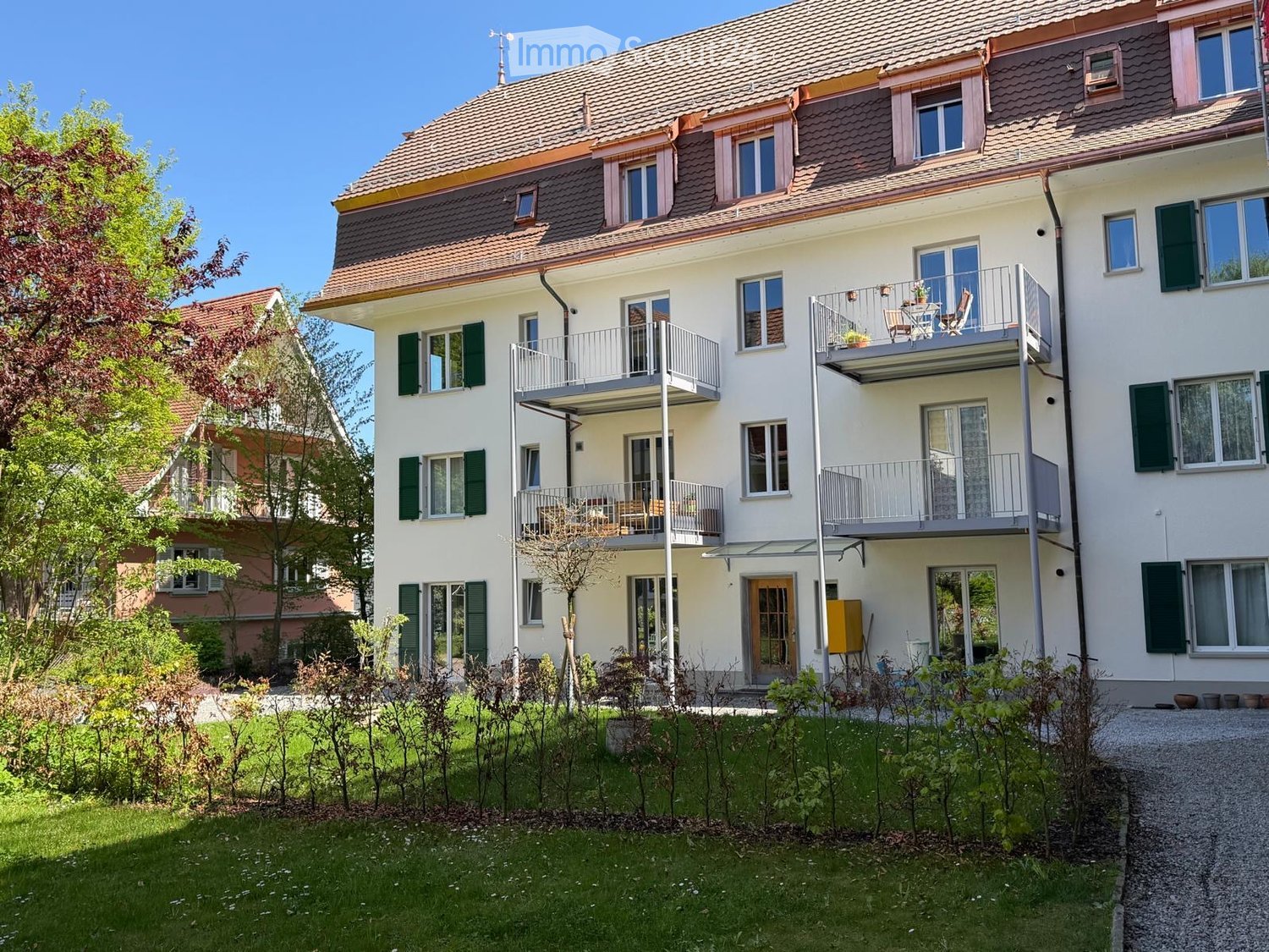 3 story apartment building, white walls, green shutters, balconies, garden, gravel driveway