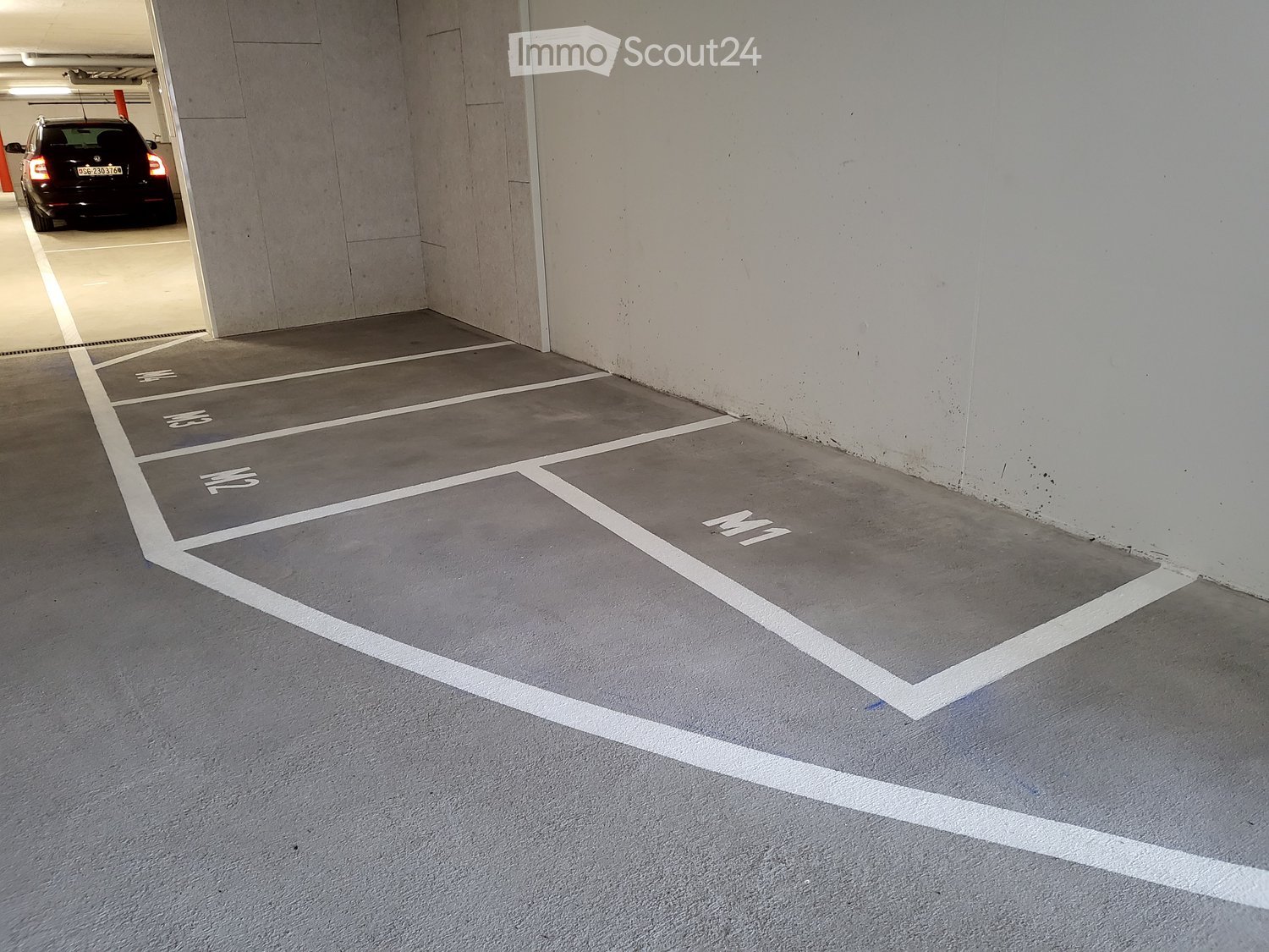 Underground parking area with white markings, grey floor, and a car parked in the distance.
