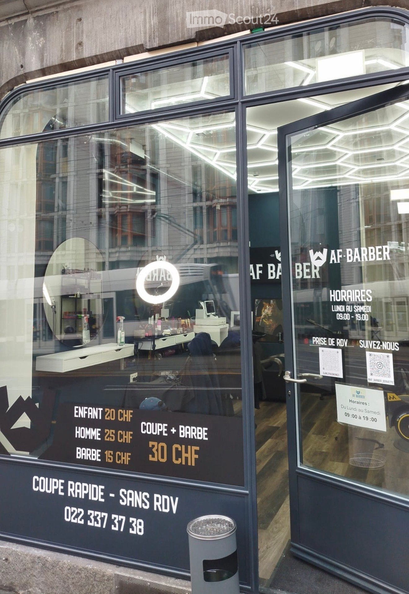 Barber shop entrance with glass door, large window, trash bin, and price list