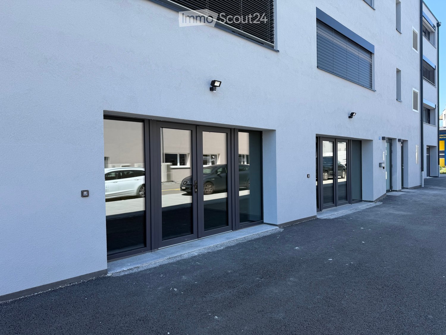 modern building with glass doors, white walls, black trim, security lights, parking area