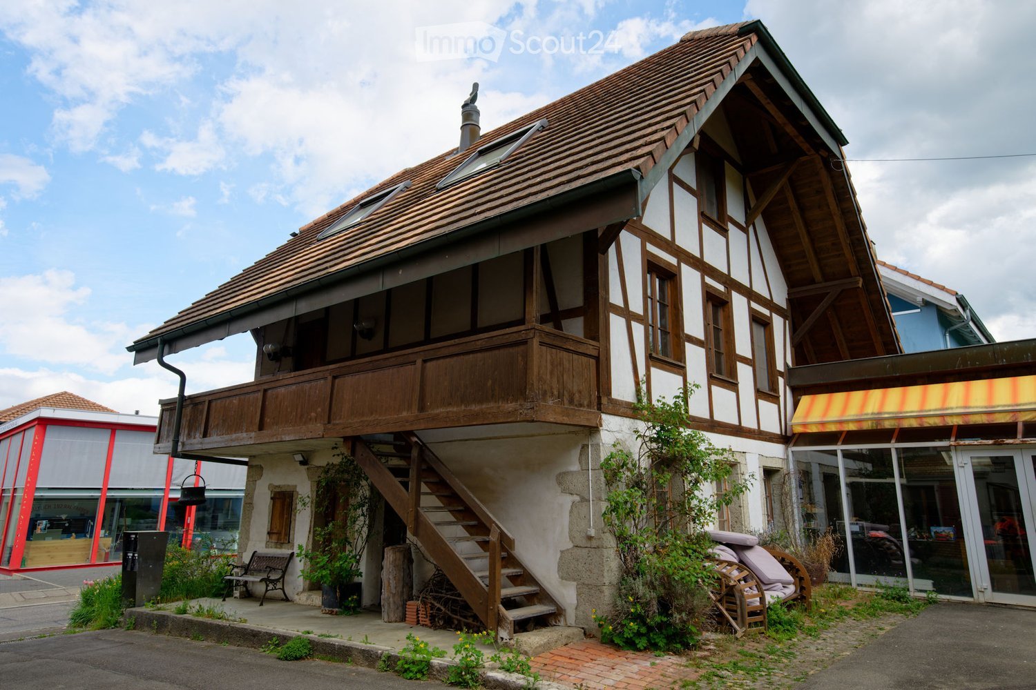2 story house, brown roof, wooden balcony, white walls, wooden stairs