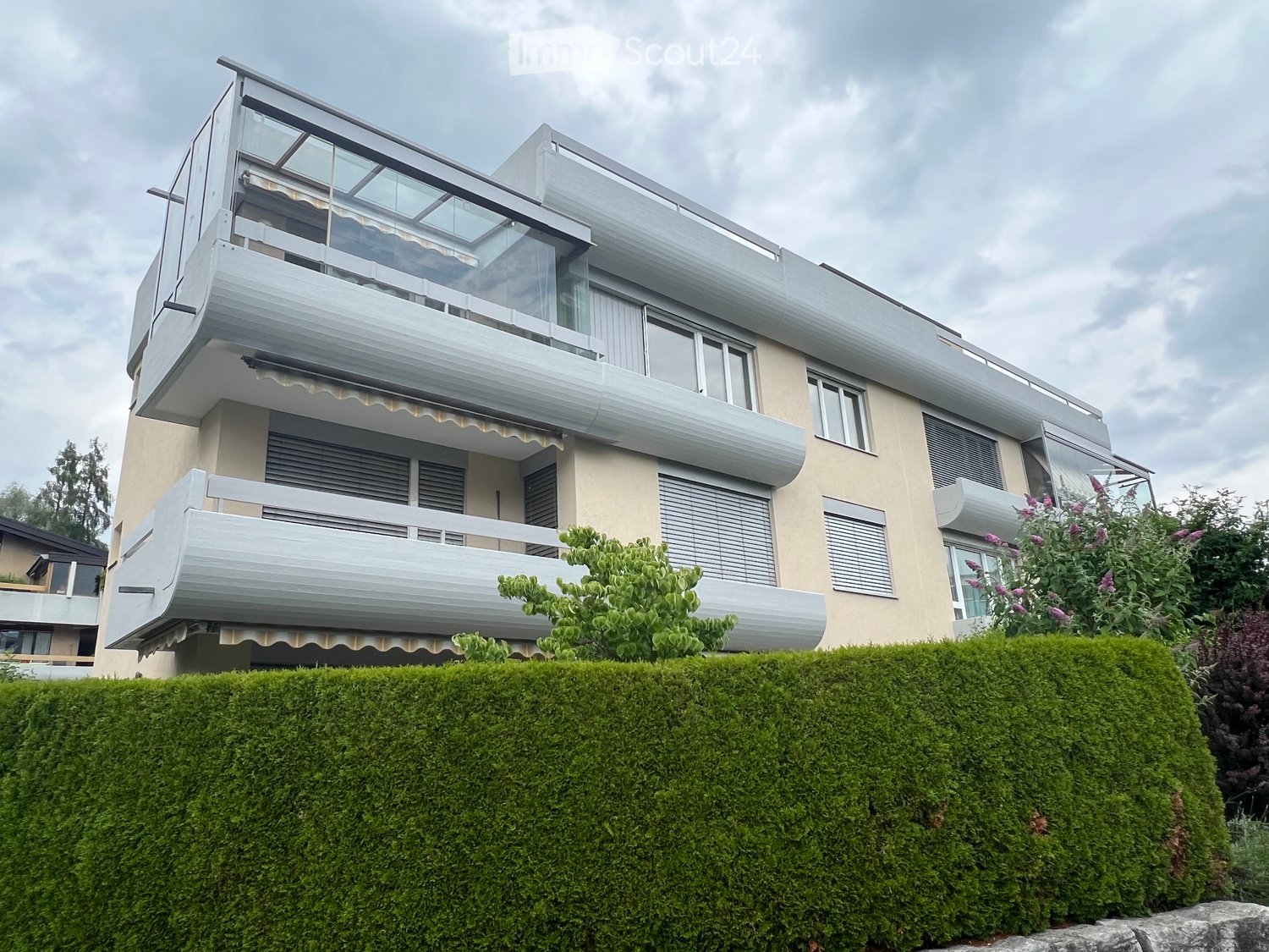3 story house, beige exterior, multiple balconies, glass railings, hedges