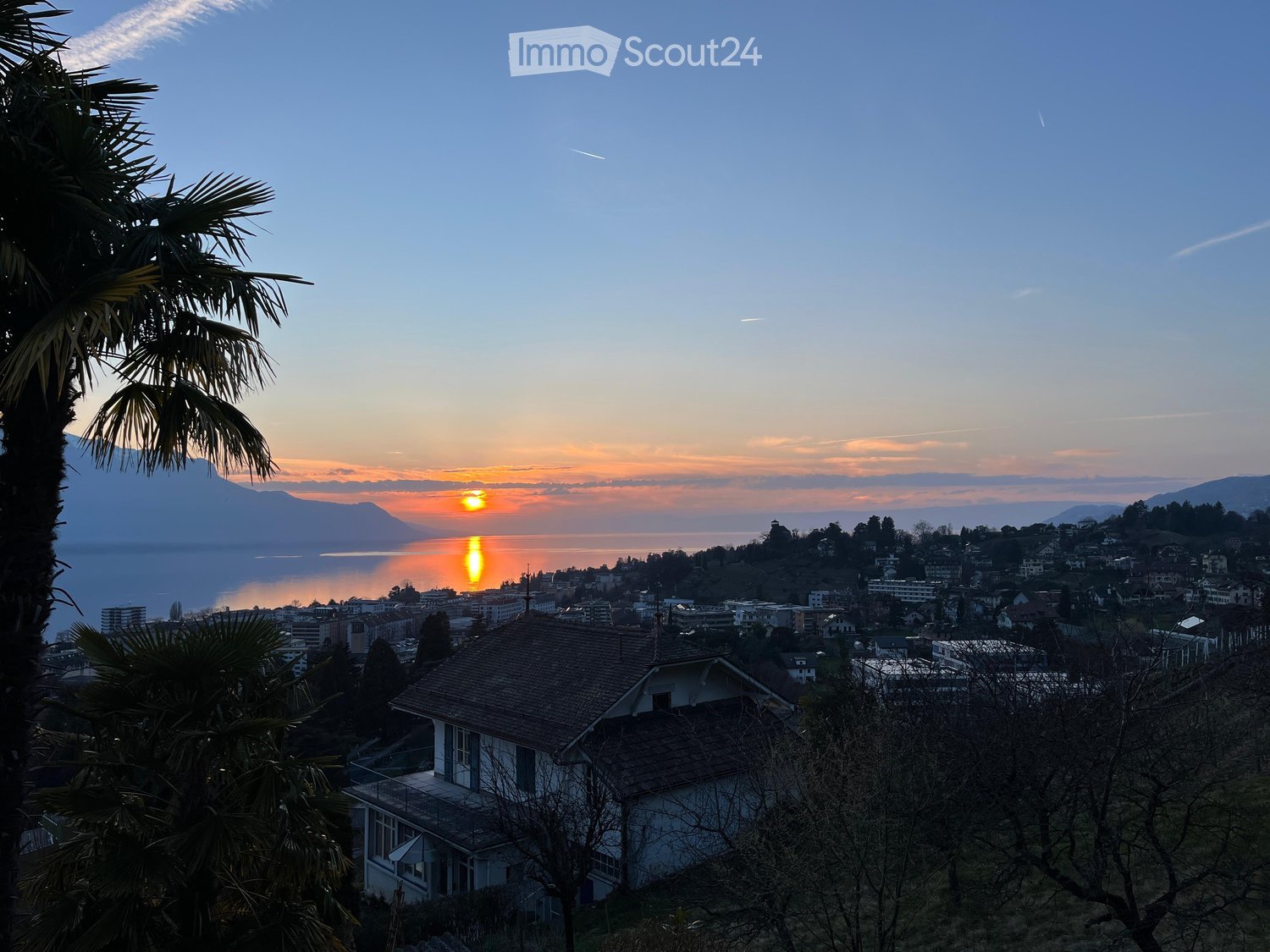 House with a view of the sunset over the lake, surrounded by trees and mountains