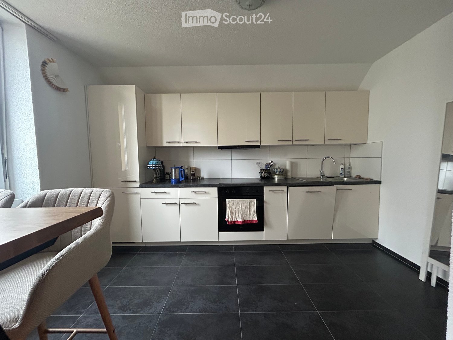 modern kitchen, white cabinets, black countertops, integrated appliances, wooden dining table, white chairs