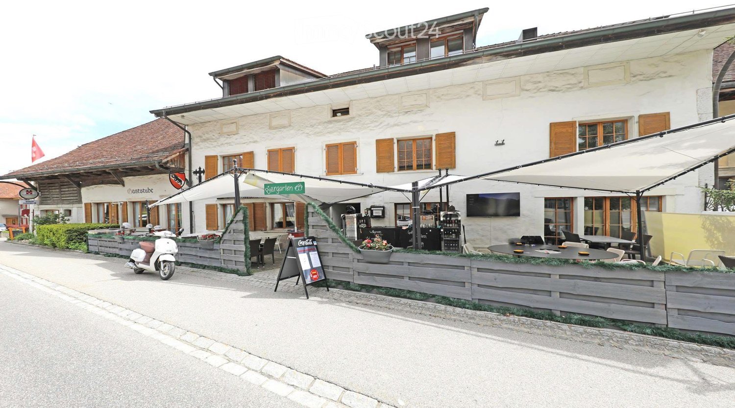 white building, wooden shutters, awnings, outdoor seating, tables, chairs, plants, scooter, flag
