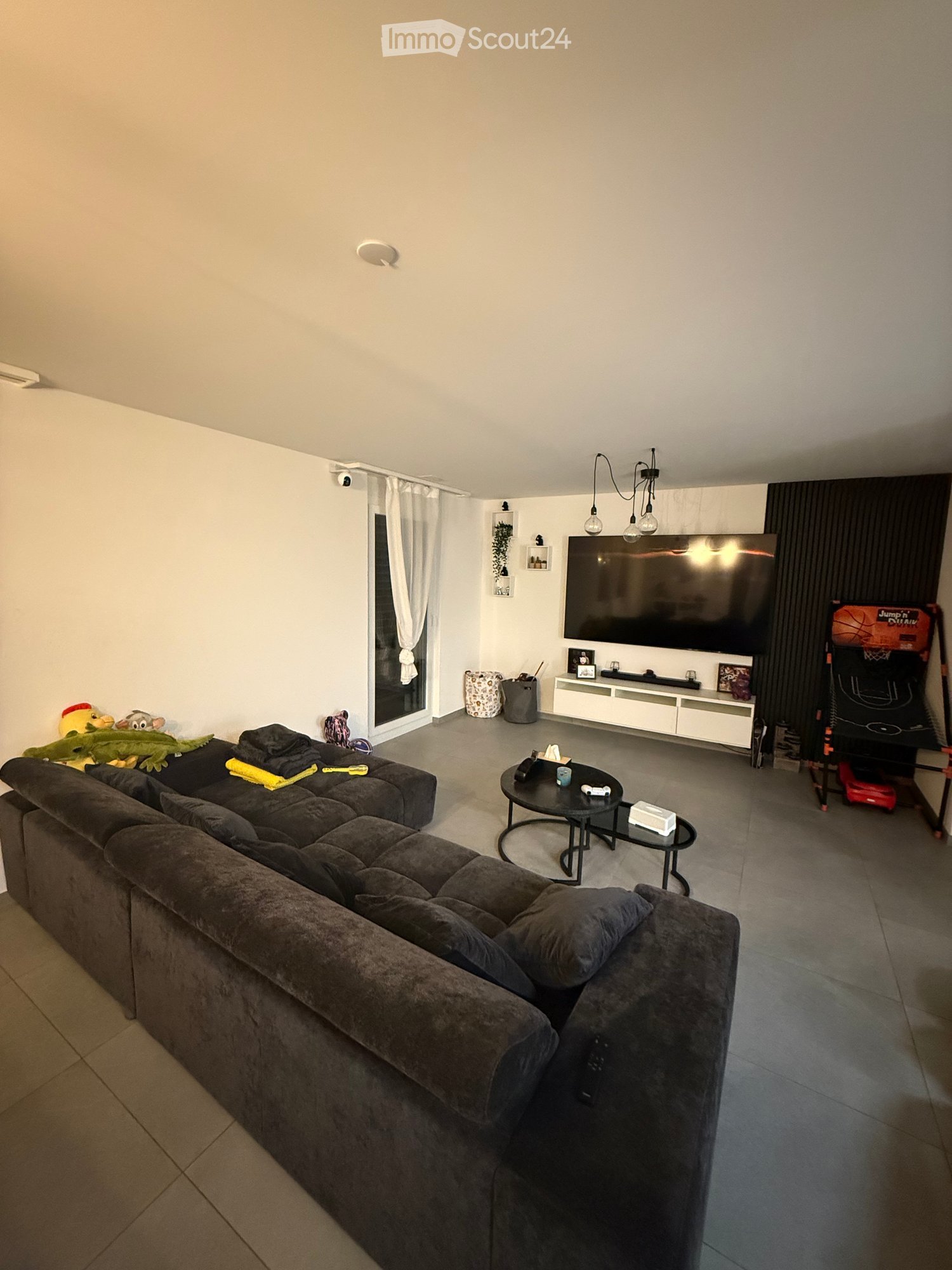 large L-shaped sofa, coffee table, TV, entertainment center, game machine, white walls, tiled floor