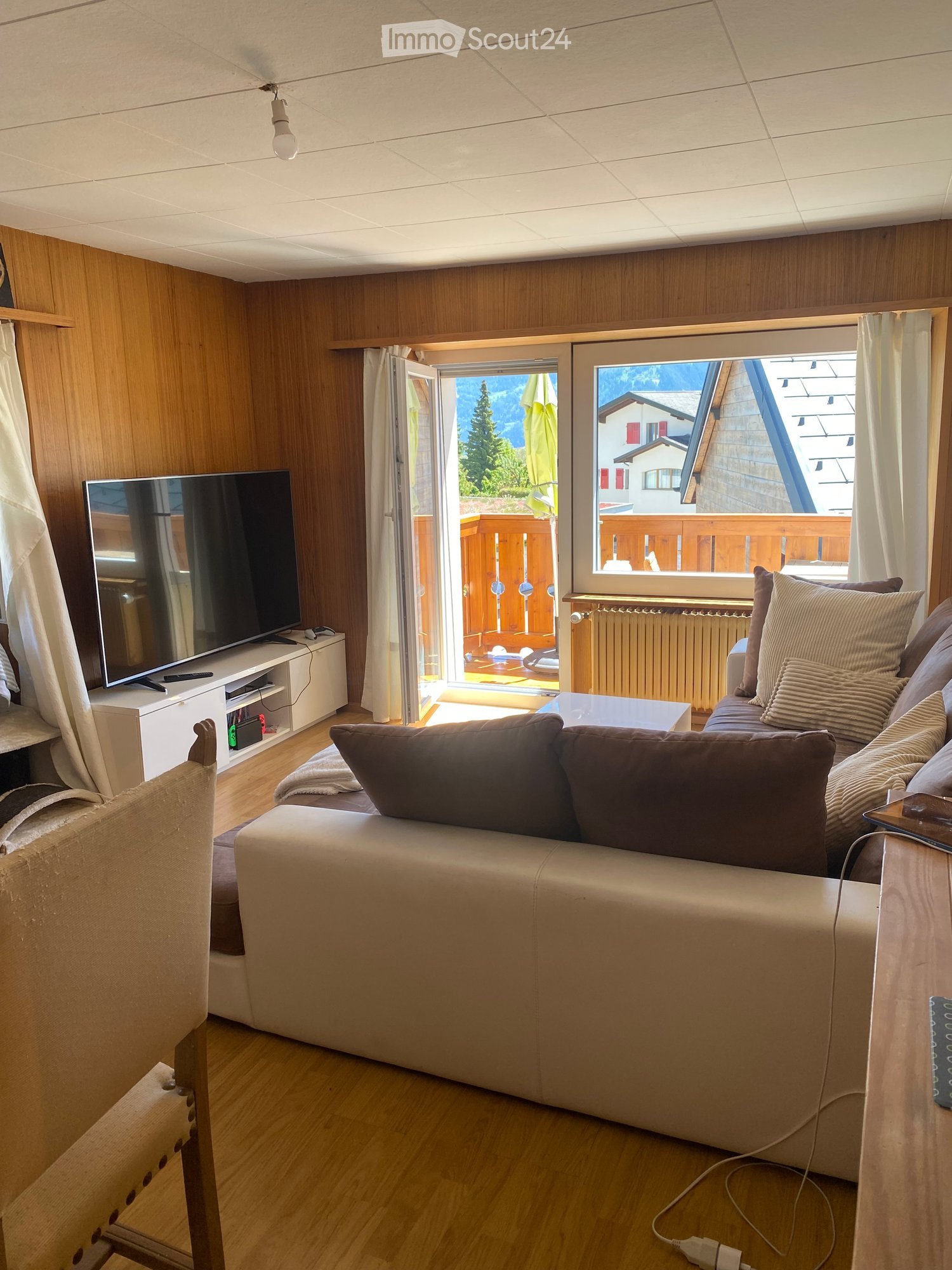 Modern living room with a large window offering a scenic mountain view, a comfortable sofa, a coffee table, a TV stand, and a chair.