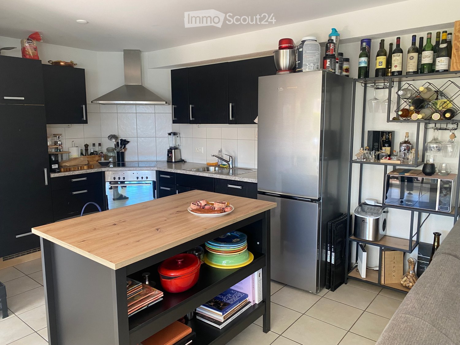 Modern kitchen with dark cabinets, stainless steel appliances, a central island, and a wine rack. The island has a wooden countertop with plates and a red pot underneath.