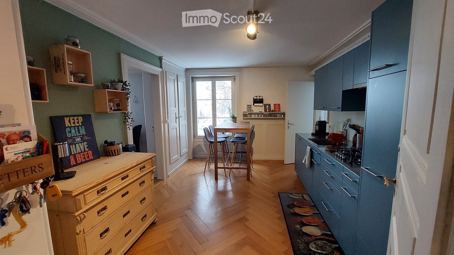 kitchen with wooden floor, wooden table, chairs, blue cabinets, wooden dresser, green wall, shelves, potted plants, light fixture