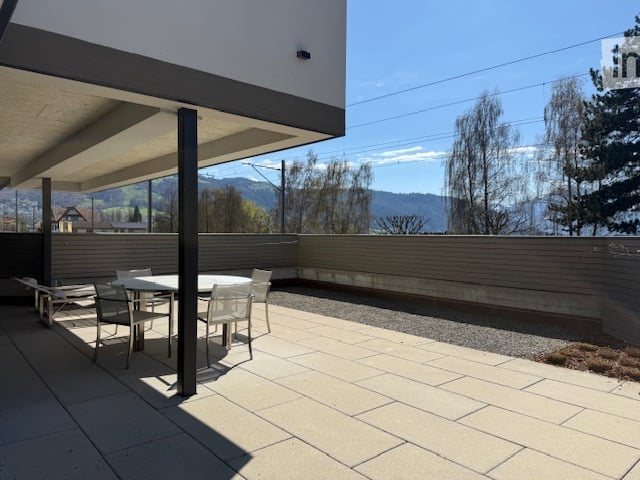 Outdoor dining area with table and chairs, tiled floor, surrounded by a low wall, with a view of the mountains