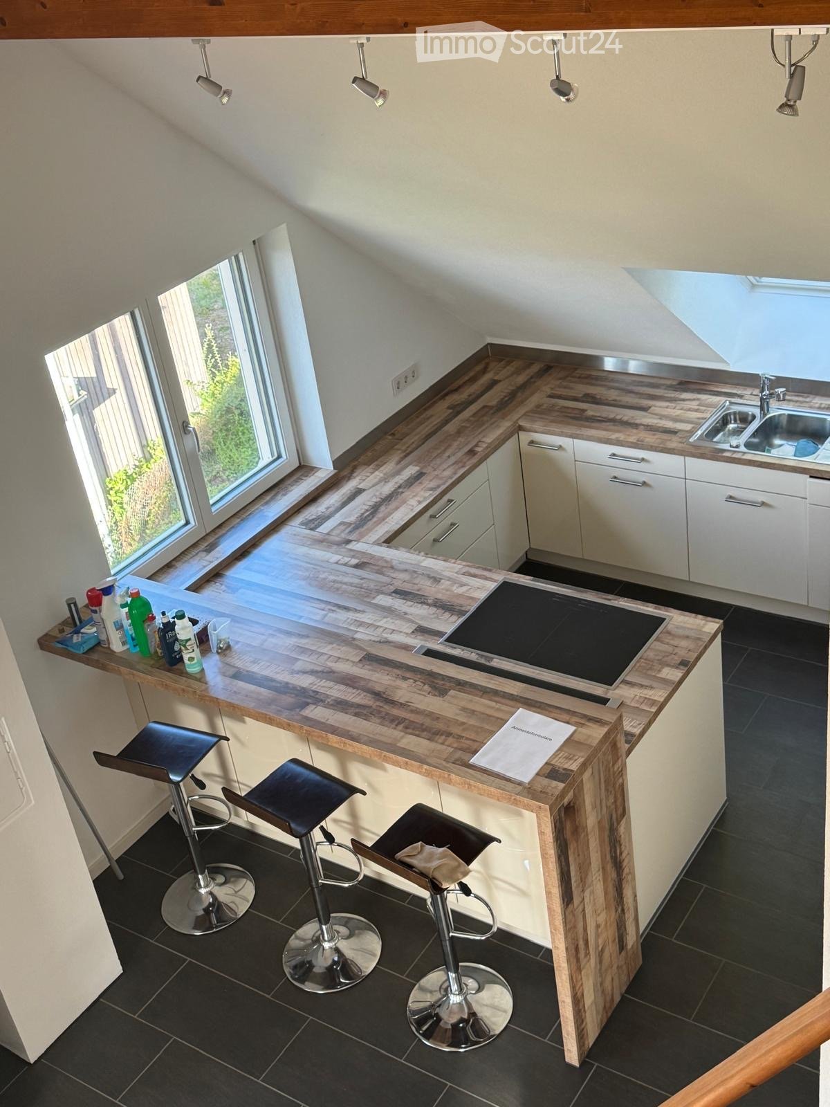 modern kitchen with wooden countertops, white cabinets, black tiled floor, induction cooktop, sink, faucet, three bar stools, and a window
