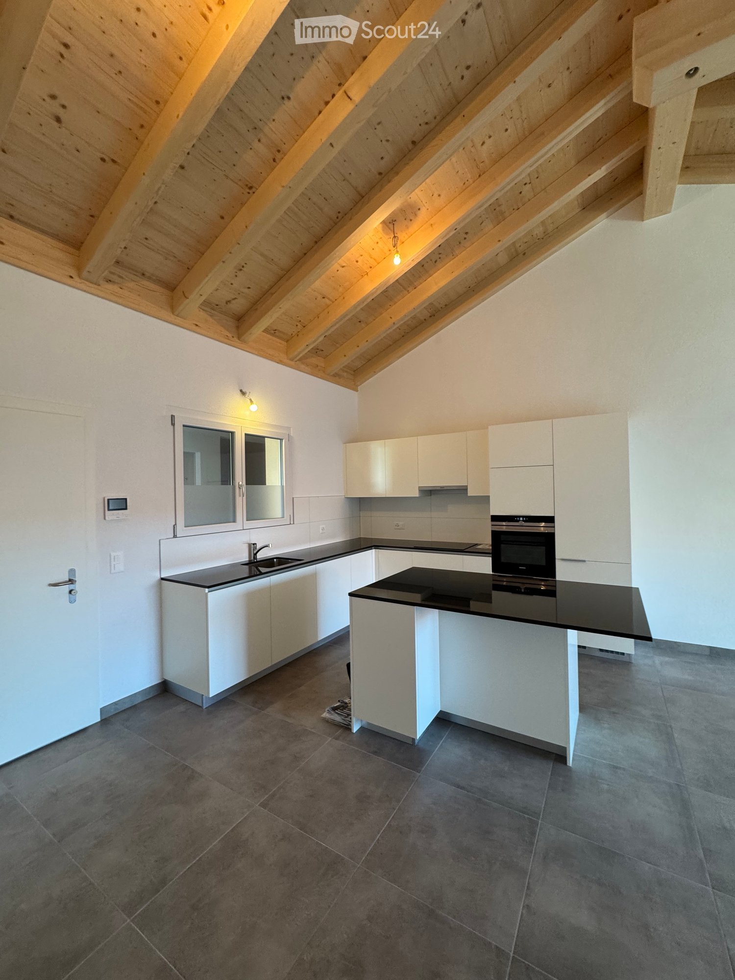 Modern kitchen with wooden ceiling, black countertops, white cabinets, central island, built-in oven, sink, and faucet, large windows, tiled floor