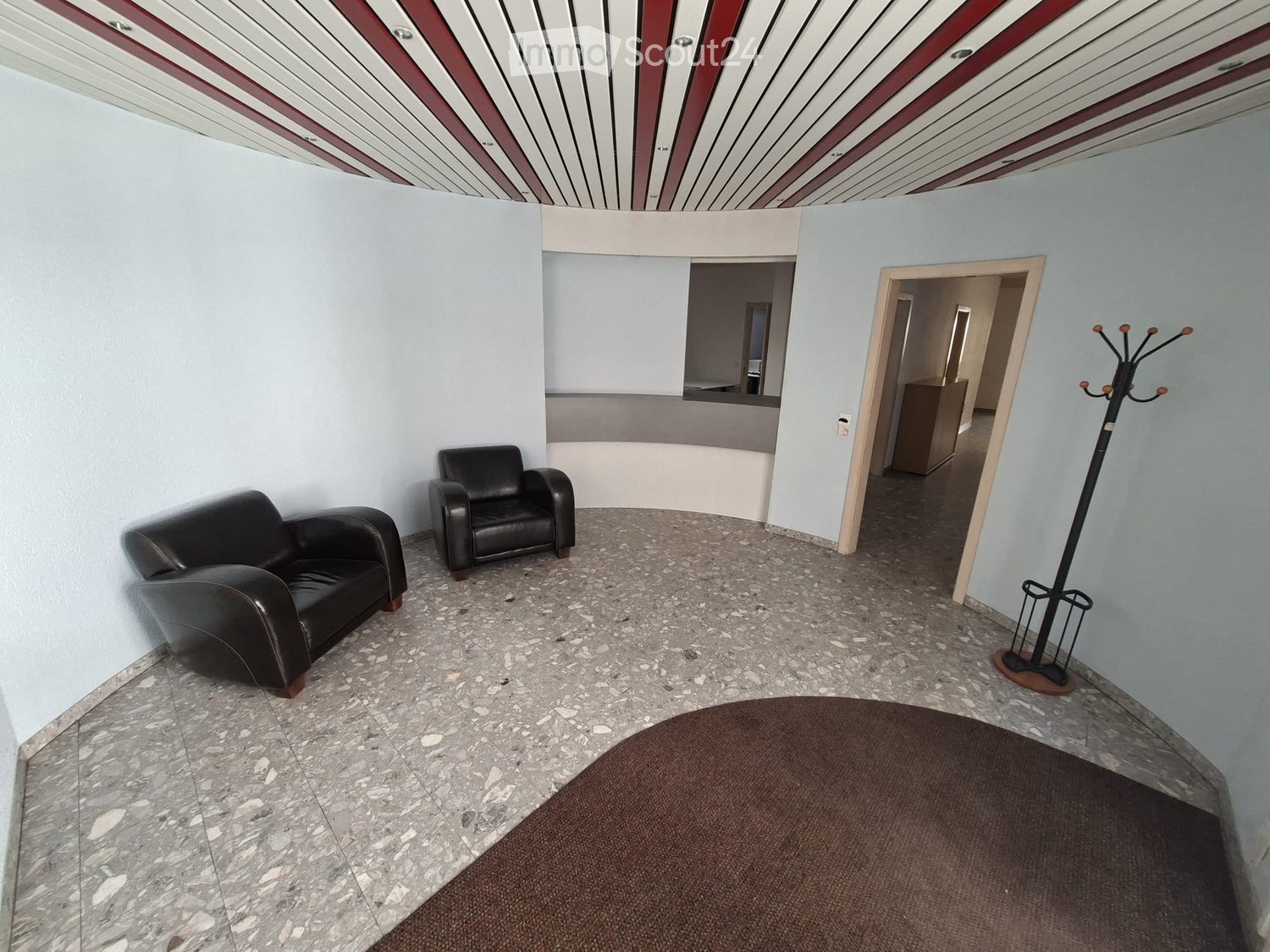 A room with two black leather chairs, a coat rack, and a marble floor.