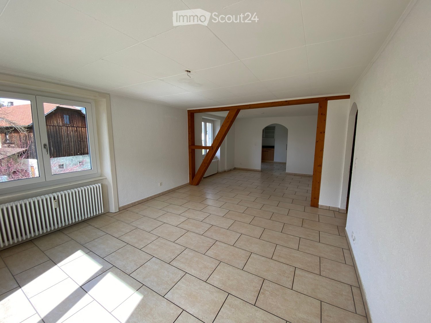 empty room, white walls, wooden beams, tiled floor, large window, radiator
