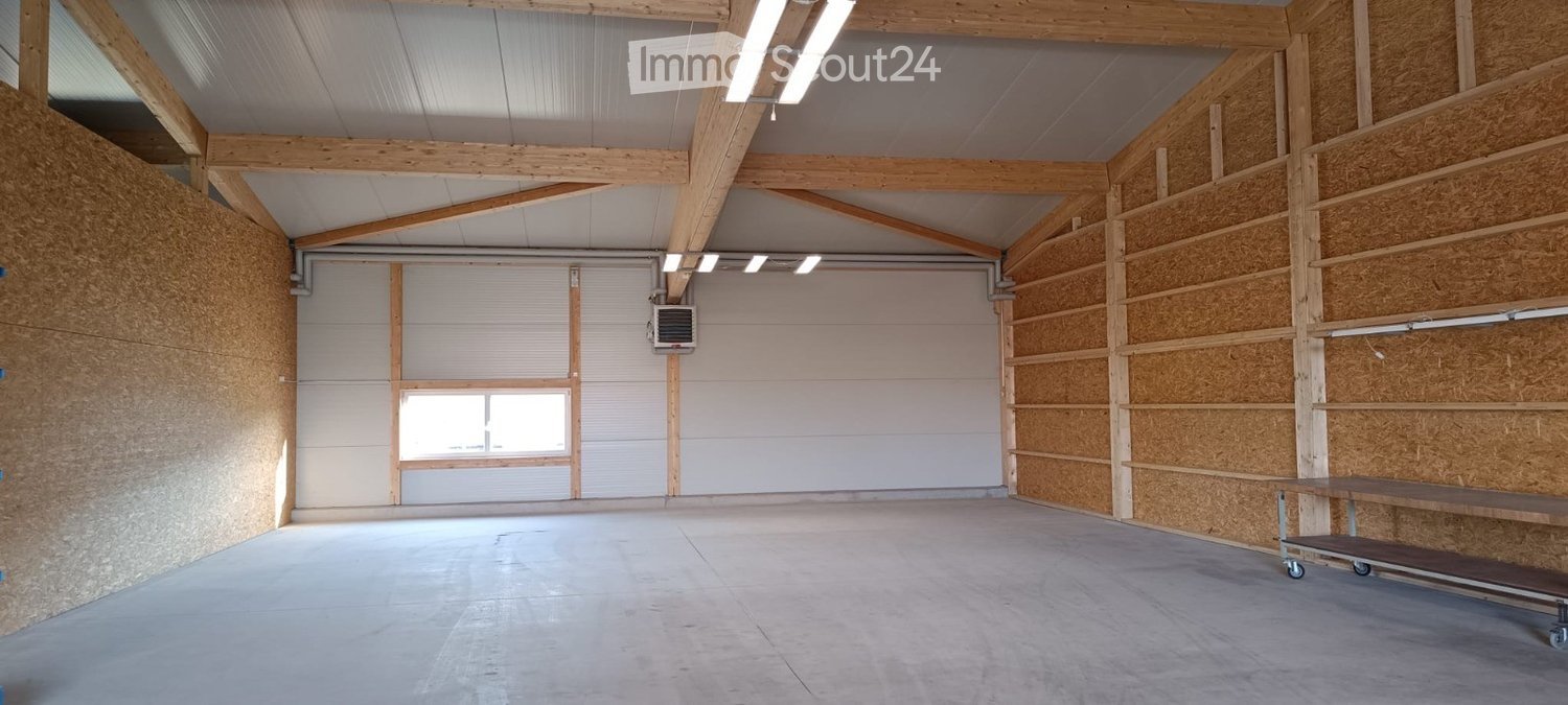 Empty garage with wooden beams, concrete floor, large garage doors, and a small window. No furniture or equipment present.