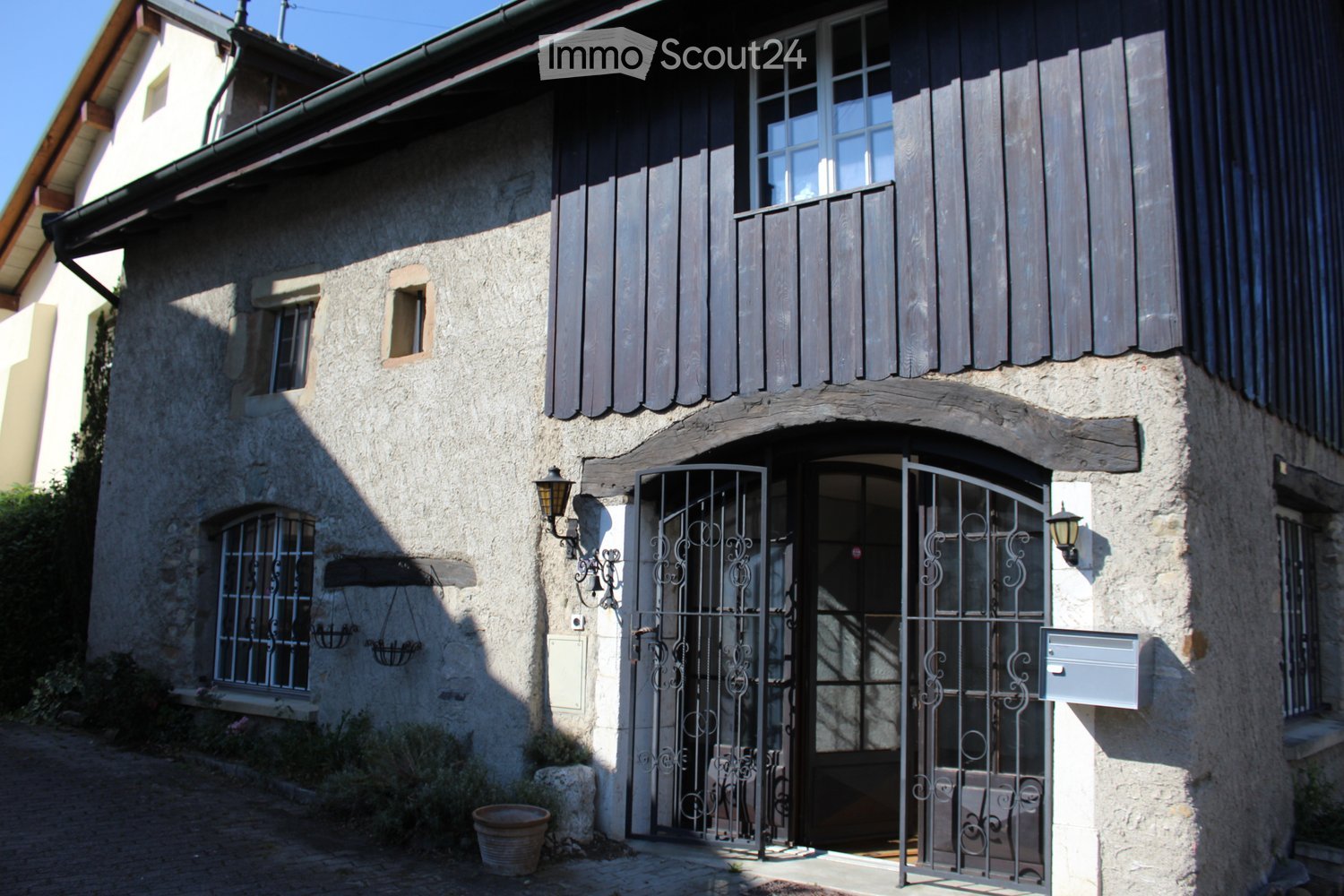 Stone house, black wooden shutters, black metal gate, lamp on both sides of the gate, mailbox on the right side of the gate