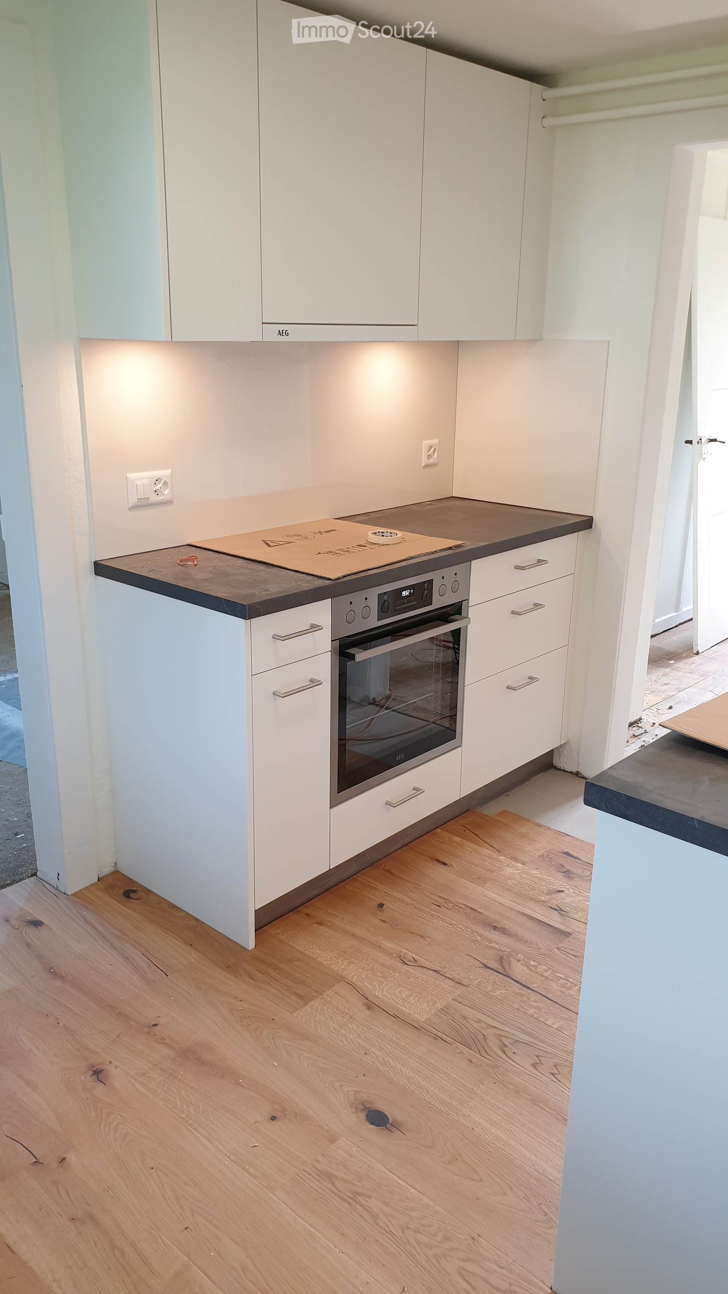 Modern kitchen with white cabinets, wooden floor, and a built-in oven.