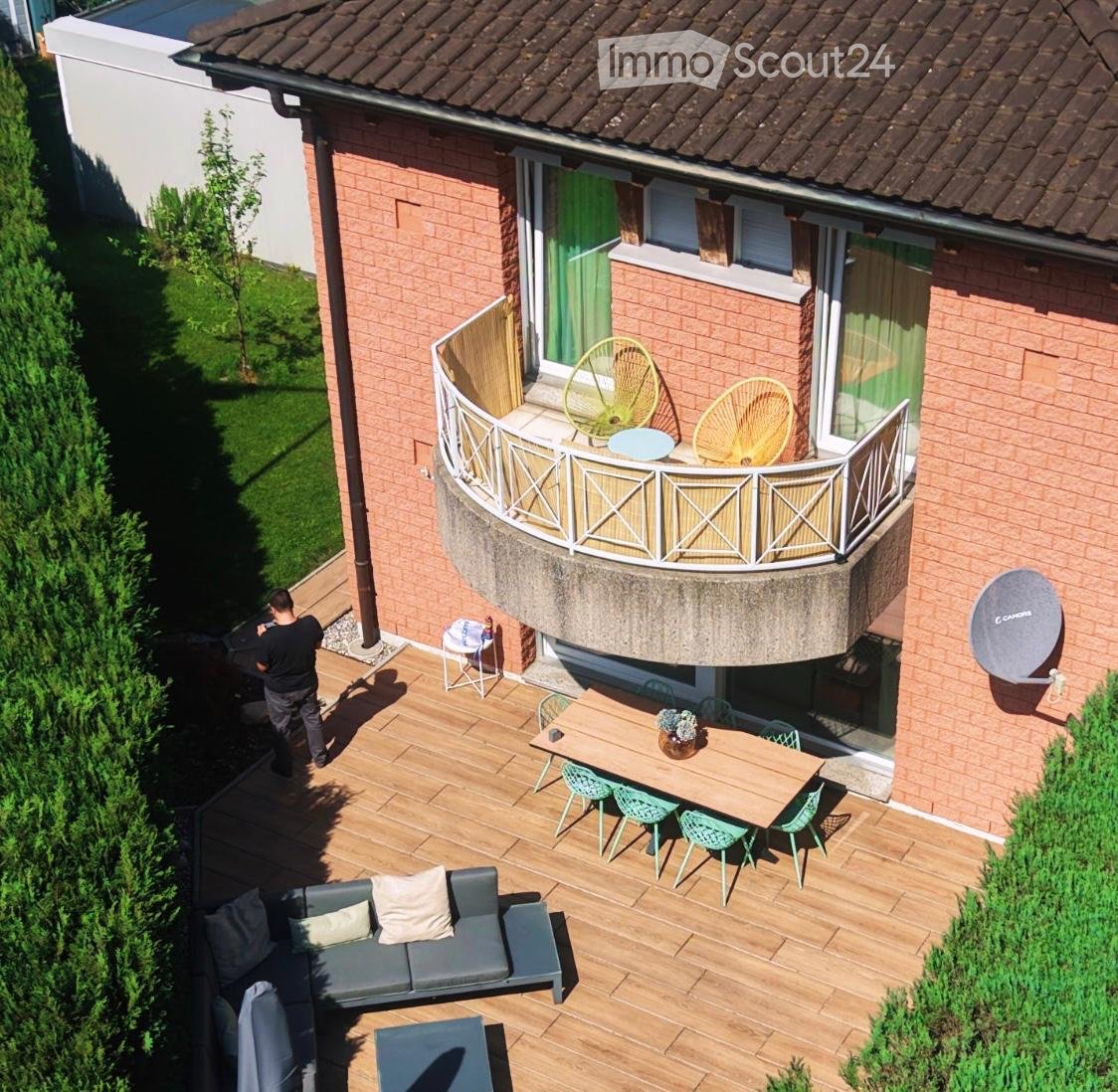 Wooden deck area with a sofa, coffee table, dining table, chairs, and a small balcony with additional seating.