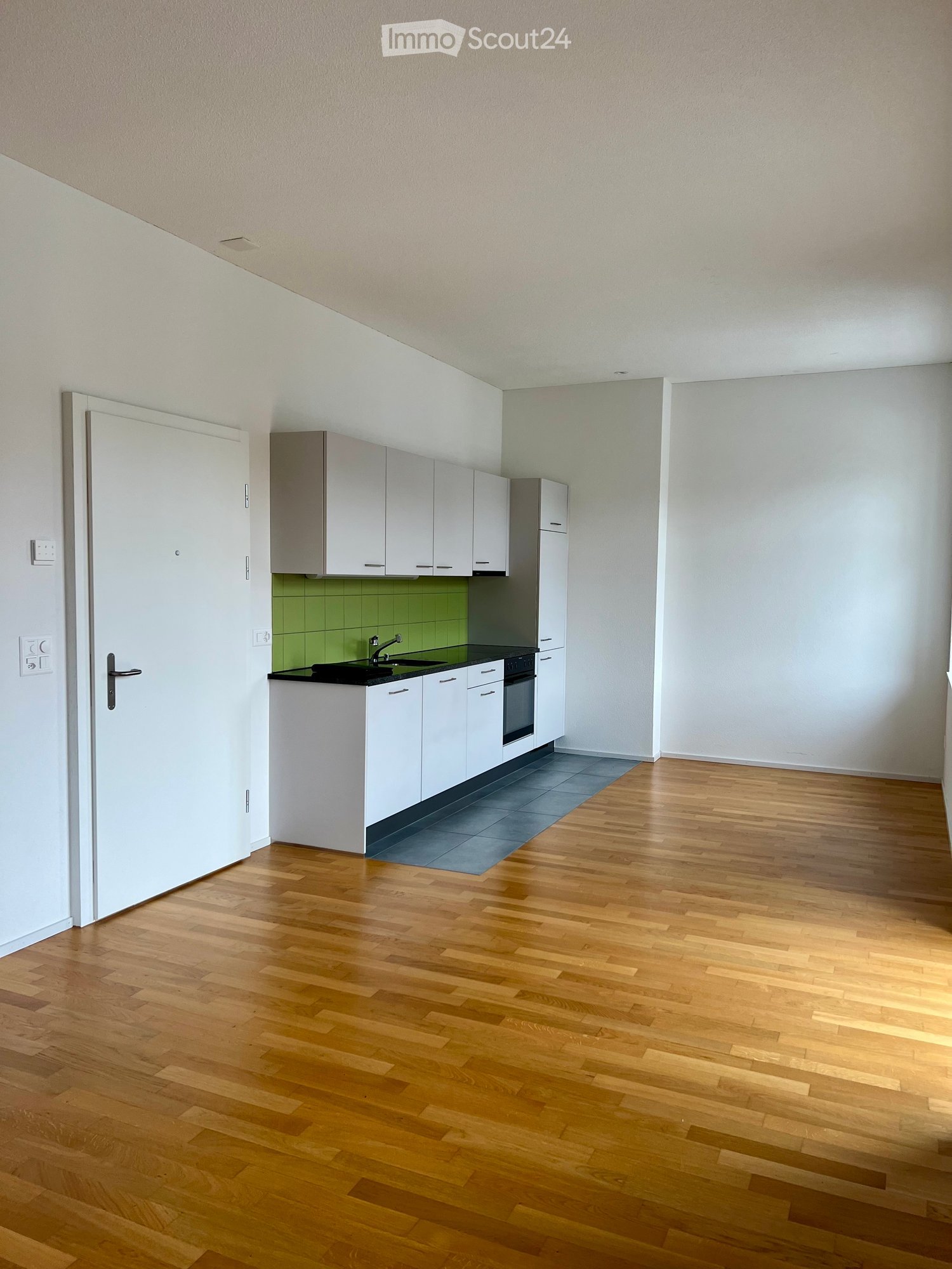 Empty kitchen with white cabinets, wooden floor, green backsplash, black countertop, sink, faucet, and appliances