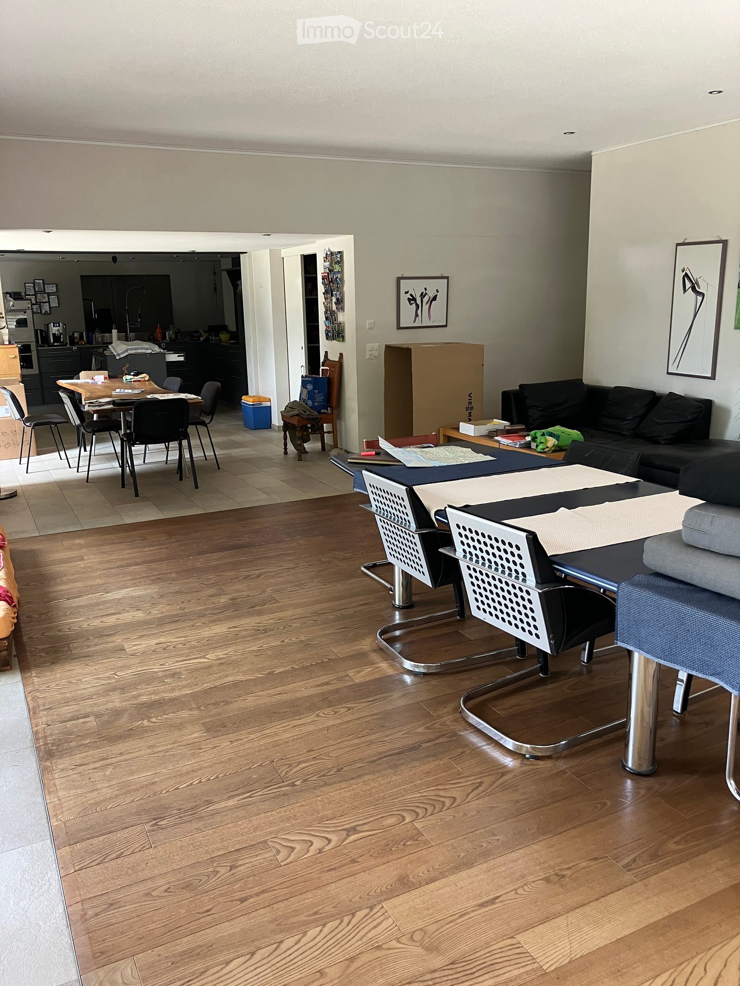Living room with hardwood flooring, a sofa, coffee table, and a dining area with a table and chairs visible in the background.