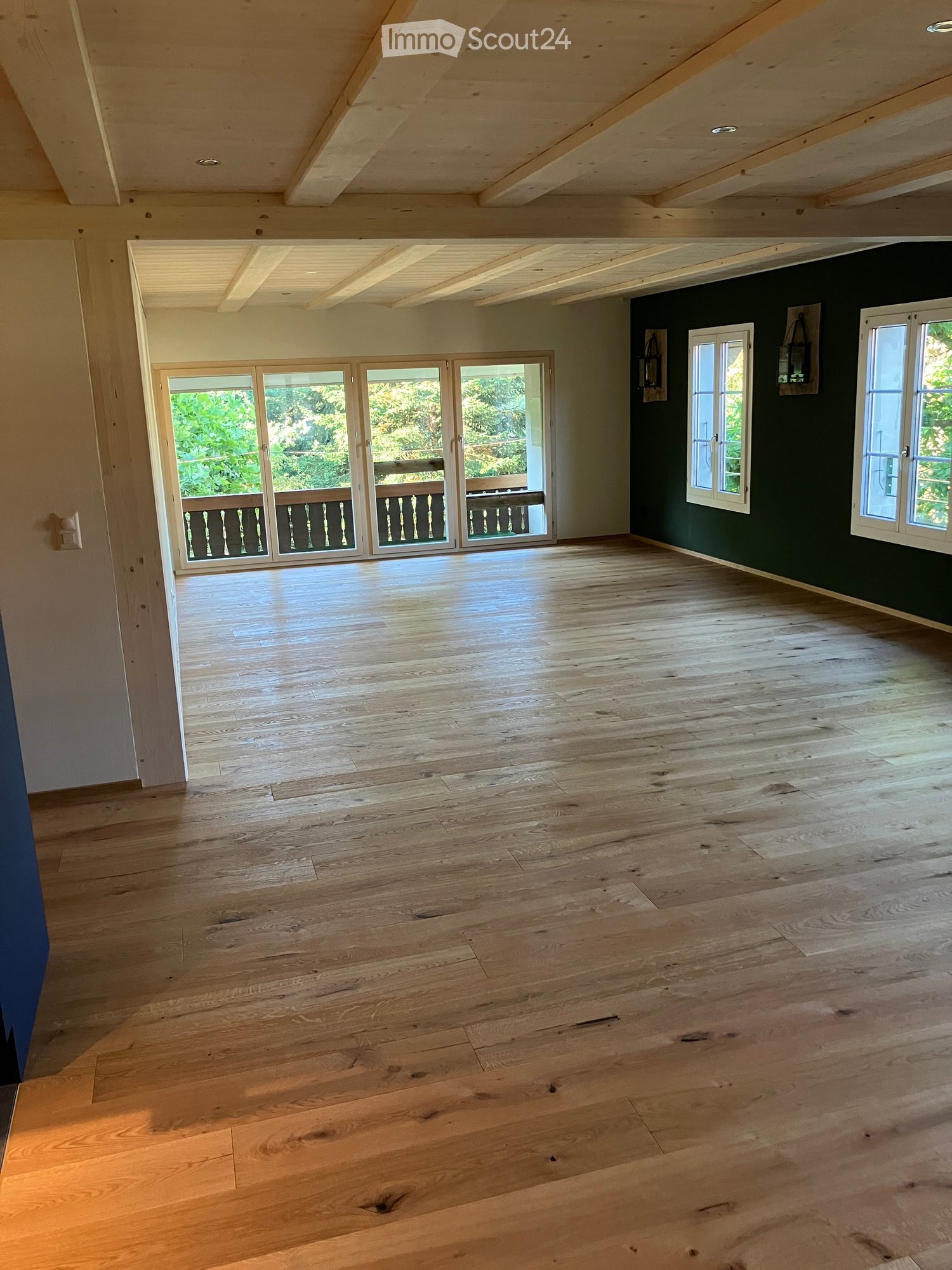 Empty room with wooden flooring, large windows, and sliding glass doors leading to a balcony.