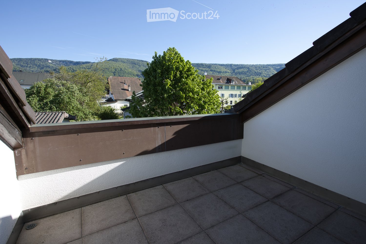 Empty terrace with tiled floor, brown railing, and a view of the town and mountains.
