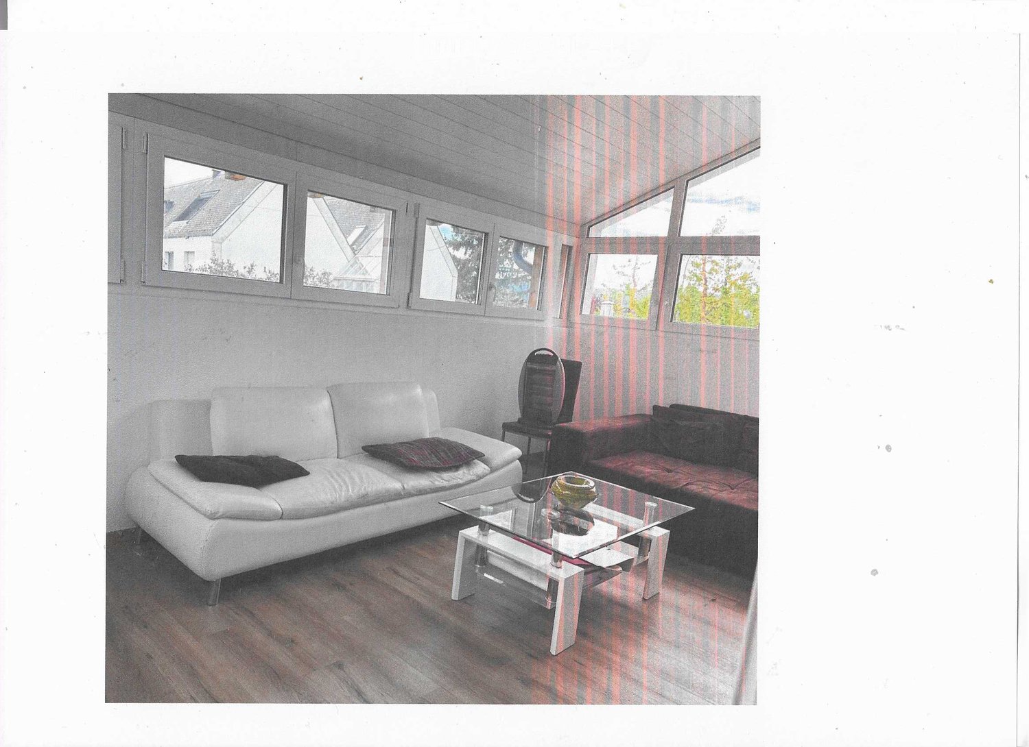 Modern living room with large windows, white leather sofa, glass coffee table, and a red patterned chair.