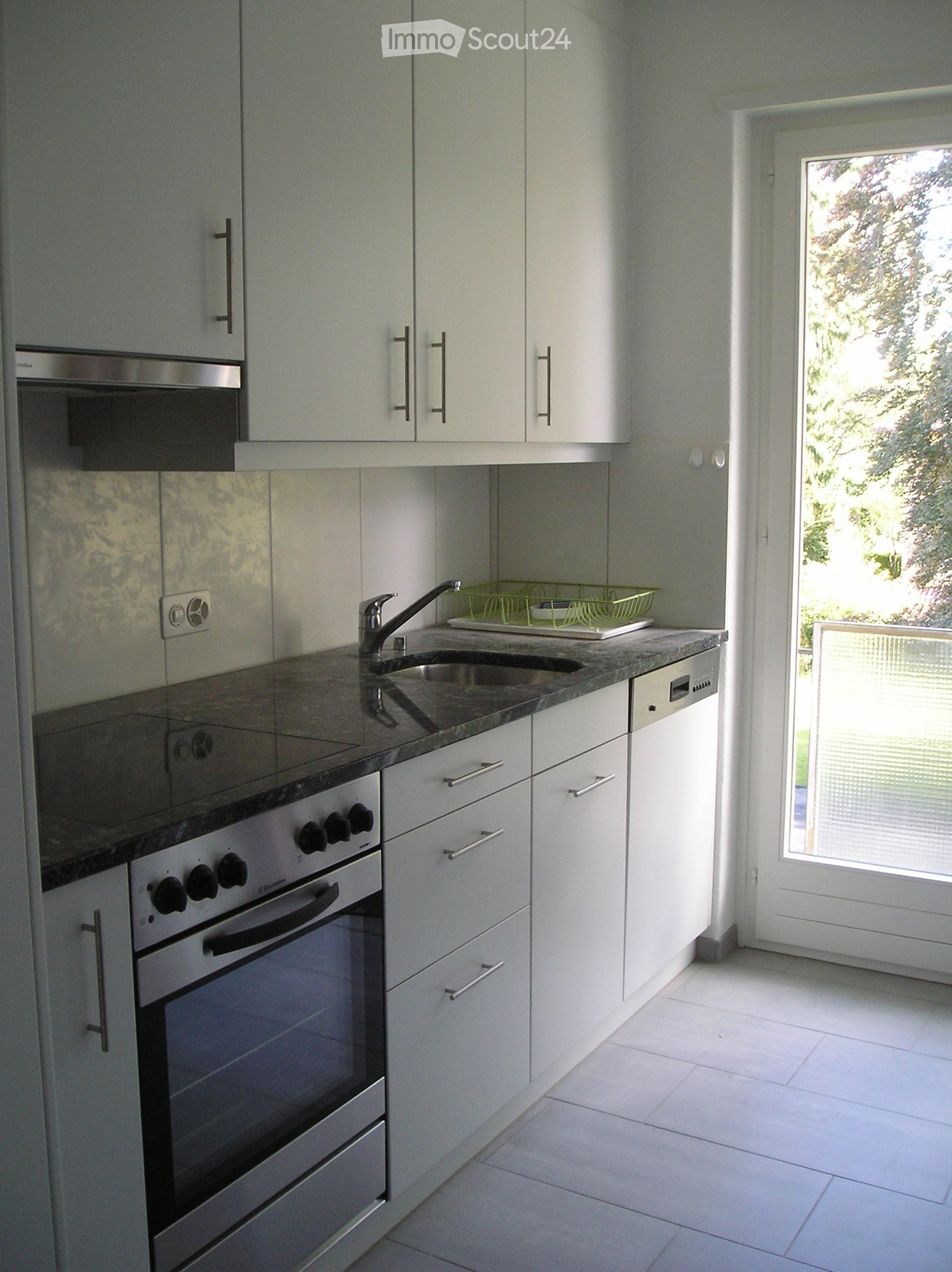 Modern kitchen with white cabinets, granite countertops, stainless steel appliances, and a glass door leading to a balcony.