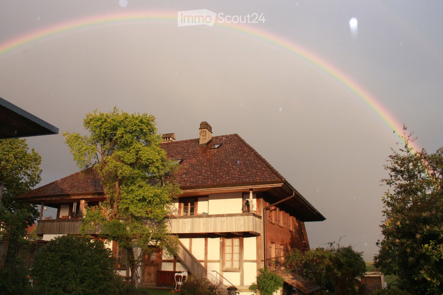 House. A two-story house with a brown roof and white walls, surrounded by trees and plants.