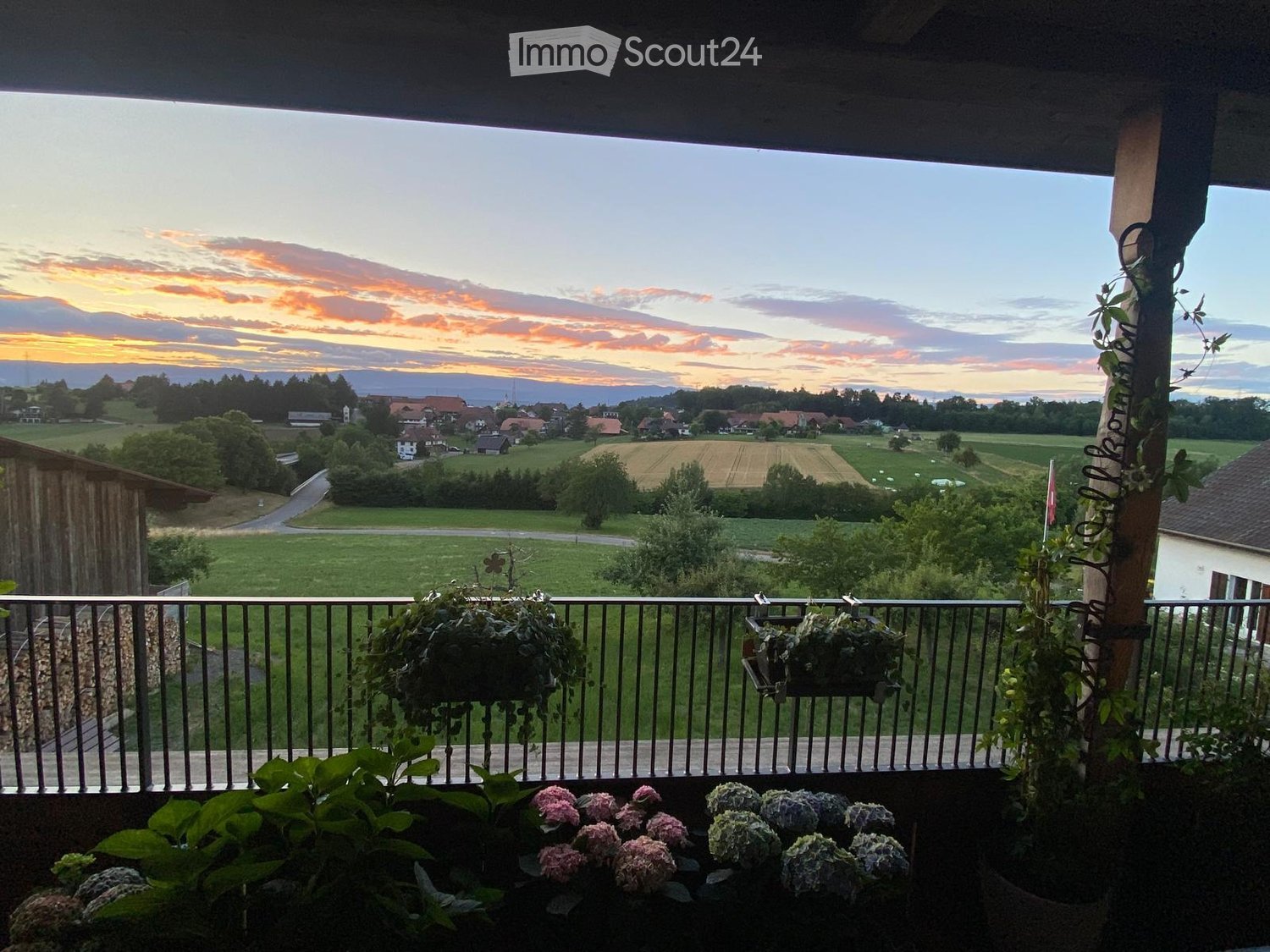 Balcony / Terrace. Balcony with metal railing, potted plants, and a scenic view of a countryside landscape at sunset.