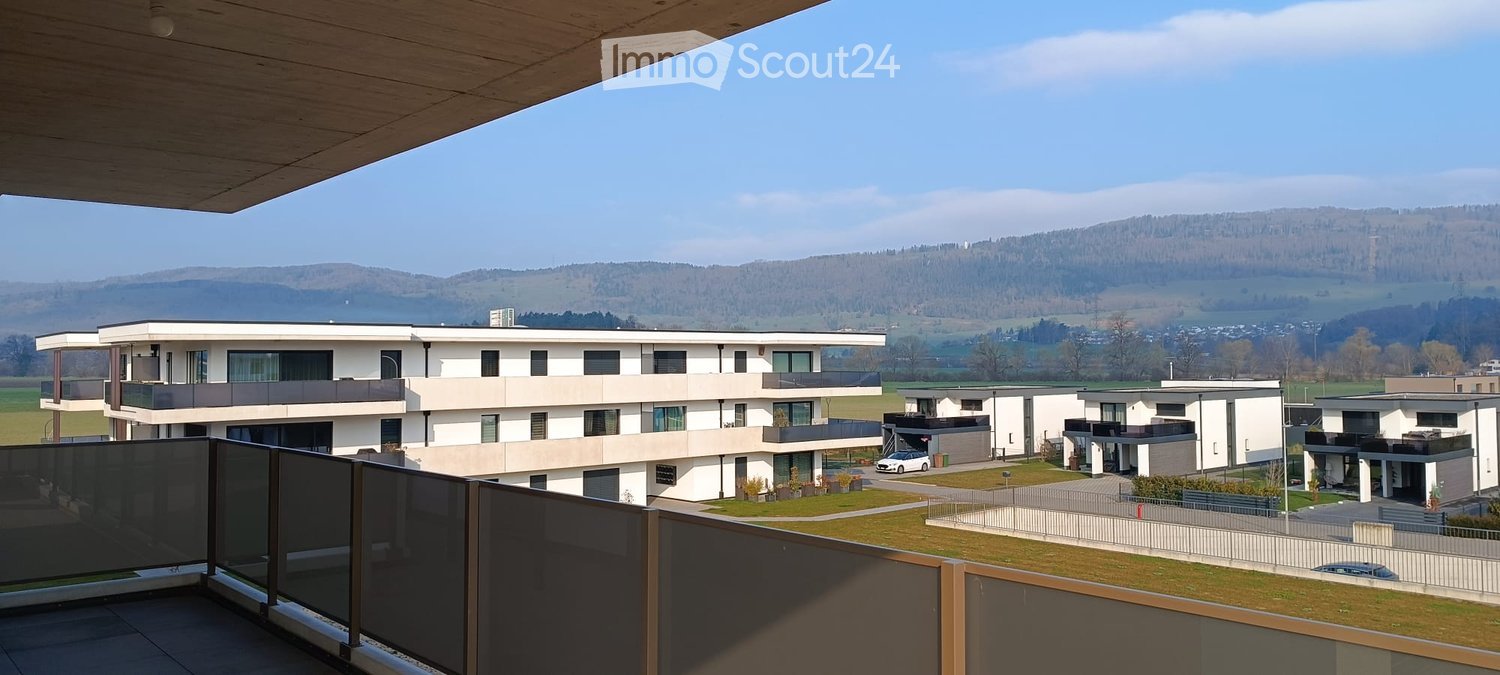 Modern apartment building with balconies, surrounded by greenery, with a view of the mountains