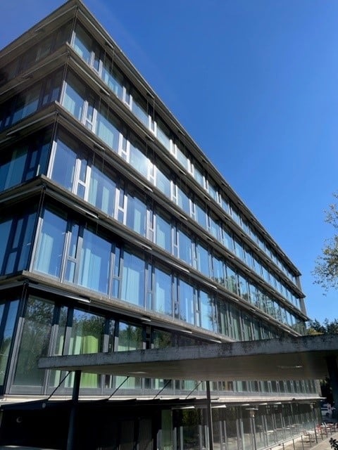 Modern multi-story building with large glass windows and a sleek, contemporary design. The structure features clean lines and a combination of glass and concrete materials.