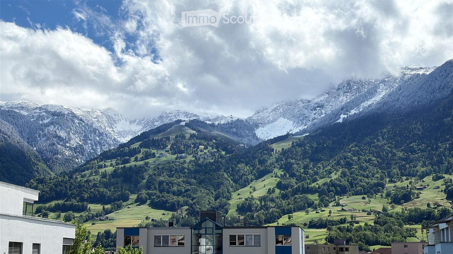 Building. Scenic view of a valley with snow-capped mountains, green fields, and scattered houses.