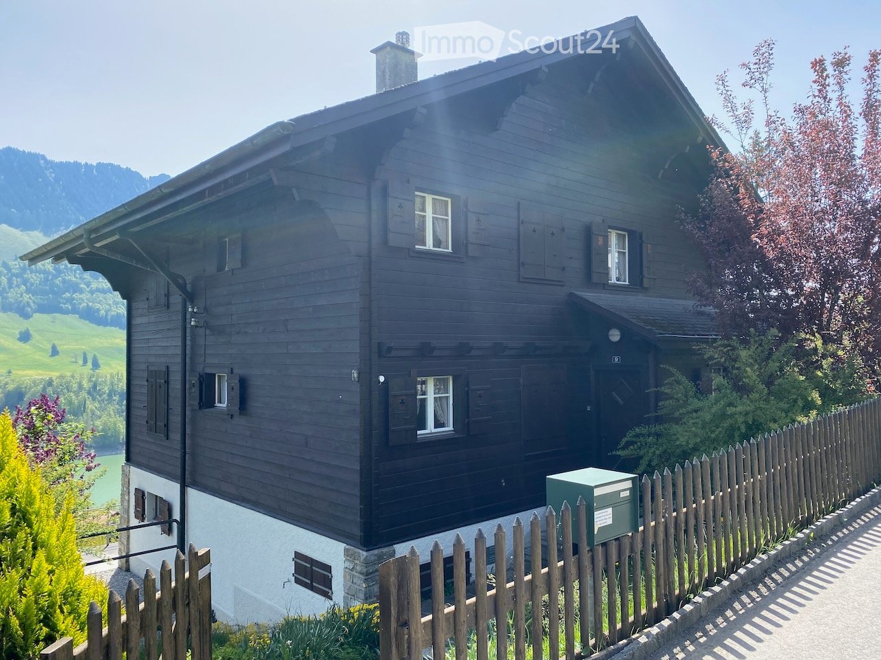 wooden chalet with a view of mountains, wooden fence, several windows, a chimney, and a mailbox