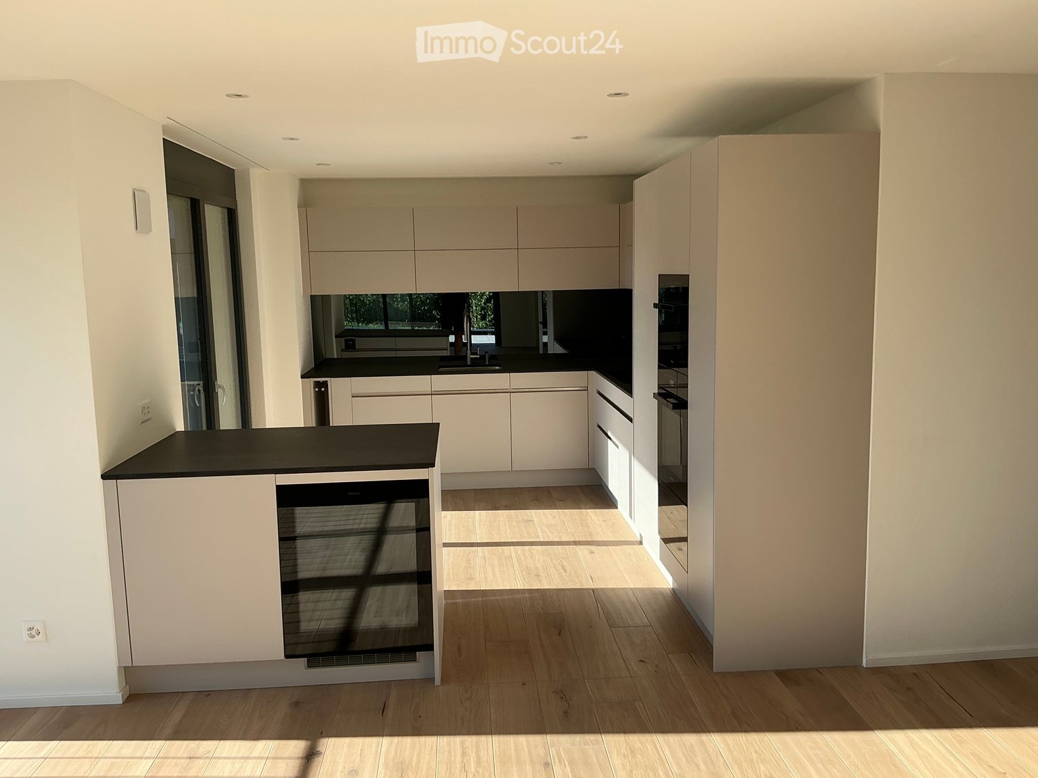 Modern kitchen with light-colored cabinets, black countertops, and wooden flooring. Features include a sink, faucet, oven, and dishwasher.