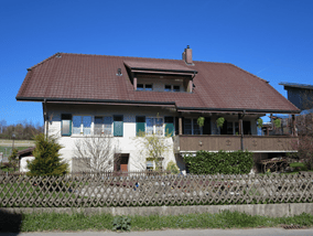 House. Two-story house with brown roof, white walls, green shutters, and a balcony on the second floor.