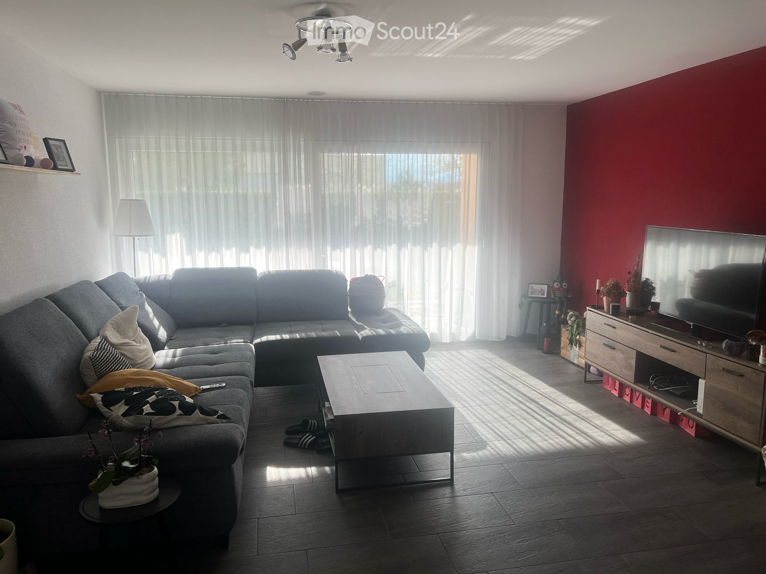Modern living room with a grey sectional sofa, coffee table, TV stand, floor lamp, and large windows with curtains.
