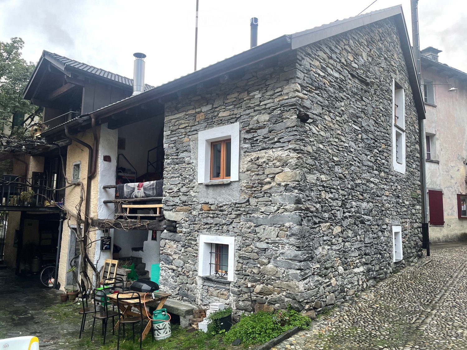 Stone house, multiple windows, balcony, chimney, outdoor seating area, bicycle