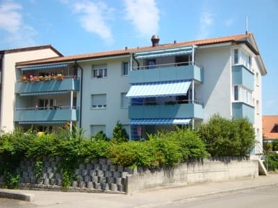 Building. Multi-story residential building with light blue balconies and awnings, surrounded by greenery.