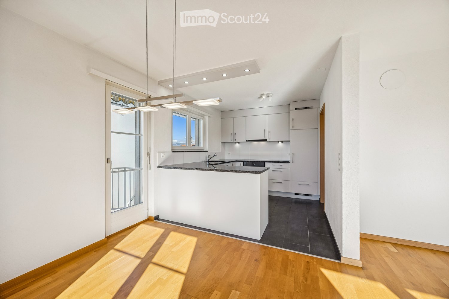 Kitchen. Modern kitchen with white cabinets, a central island, and a black countertop. The space features wooden flooring and large windows that allow natural light to fill the room.